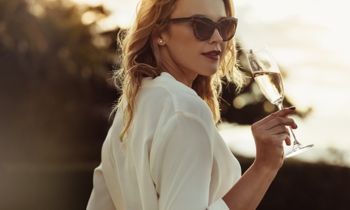 a woman sipping on wine outdoors in a bright dress
